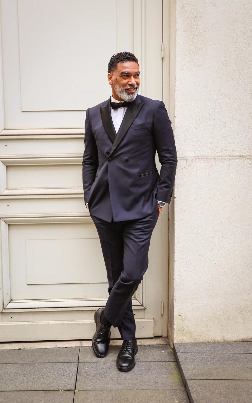 Man in dark blue suit by a beige wall